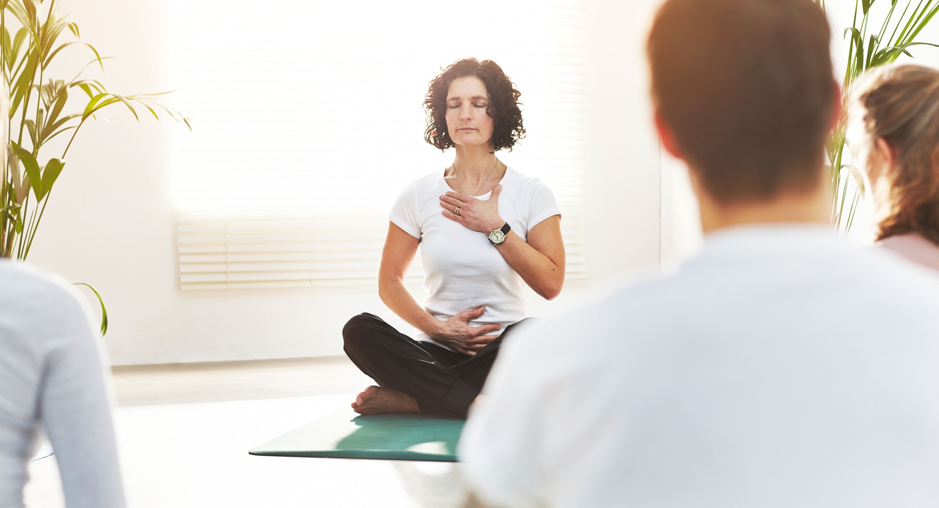 Yoga instructor training people in a fitness class in studio. Yogi teaching pranayama breathing techniques with hands on chest and belly. Practicing mindful meditation for zen energy in lotus pose